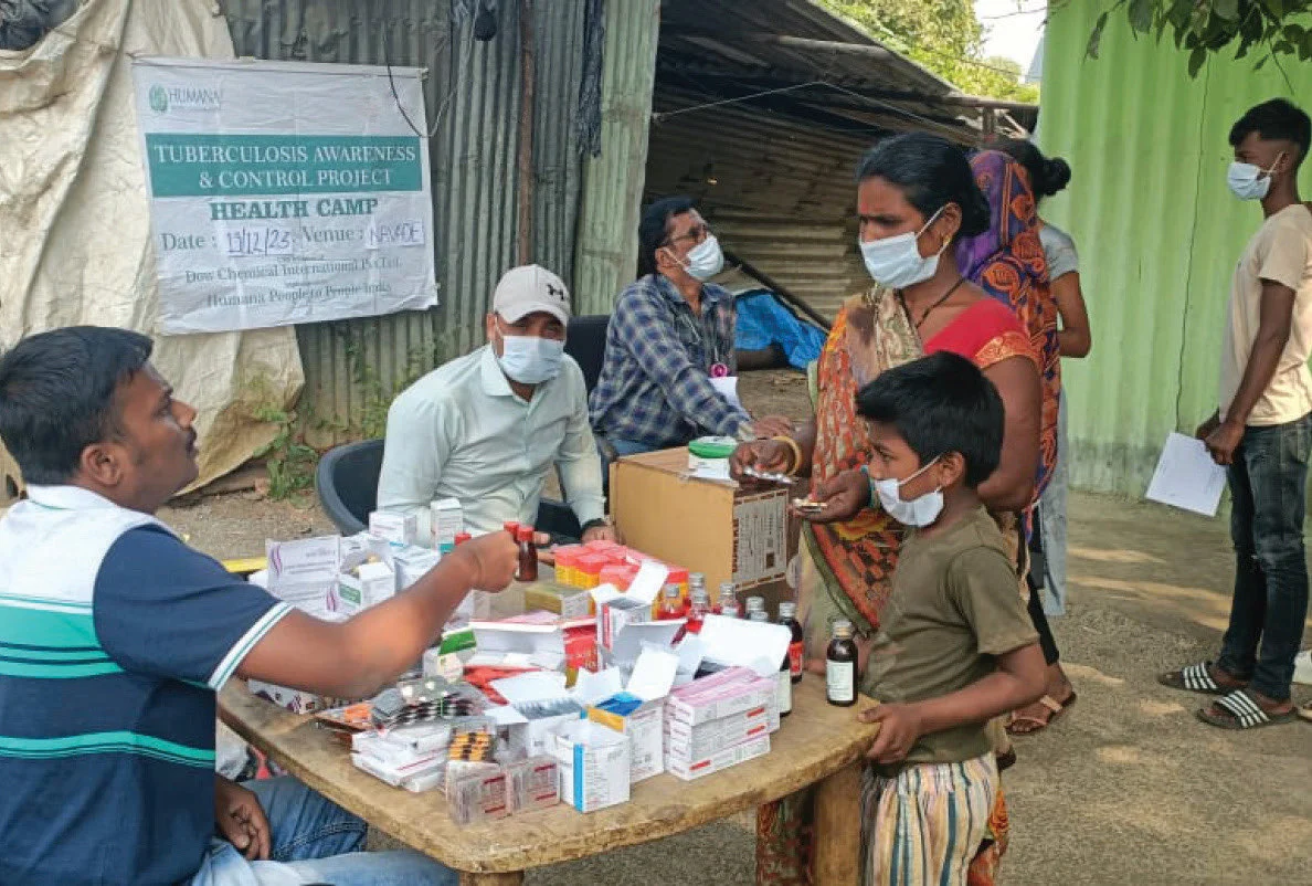 A community health camp with a clinician, supplies, and people receiving care.