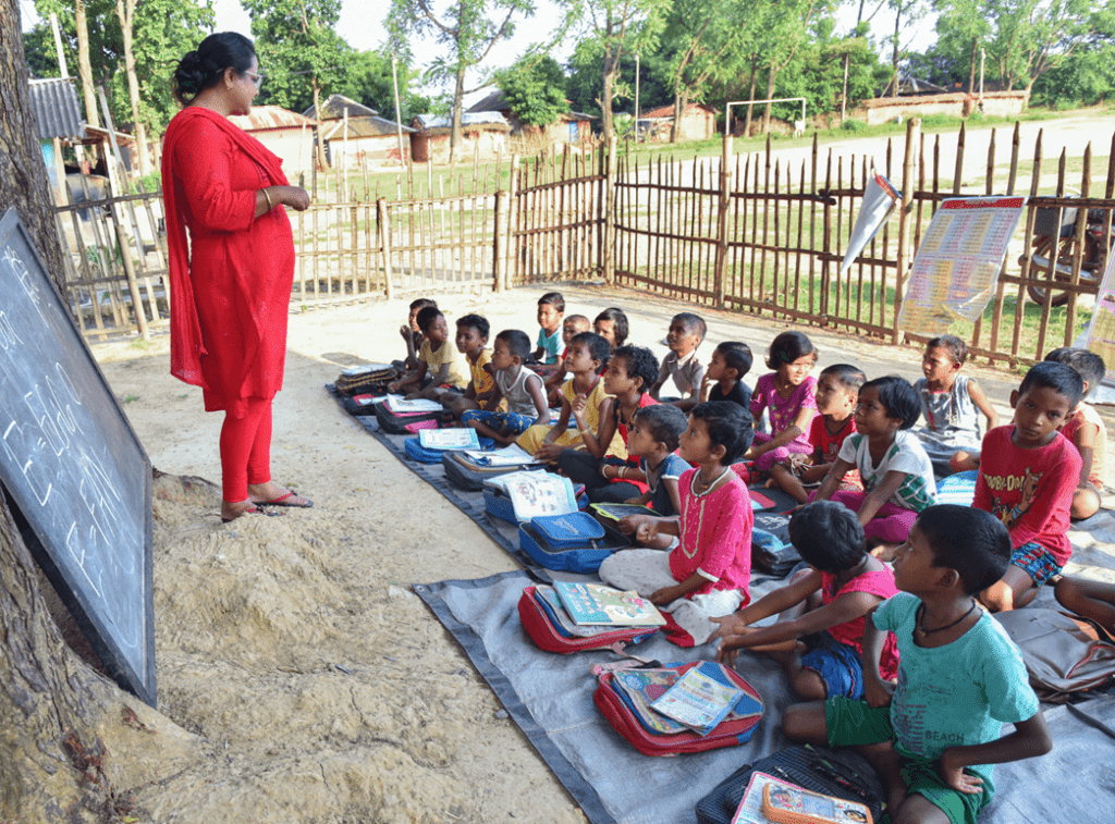Children gathered for an outdoor learning session with a facilitator and school materials.